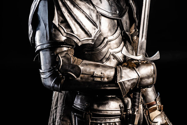 Cropped view of knight in armor holding sword isolated on black