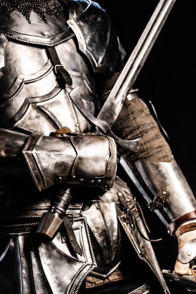 cropped view of knight in armor holding sword isolated on black 