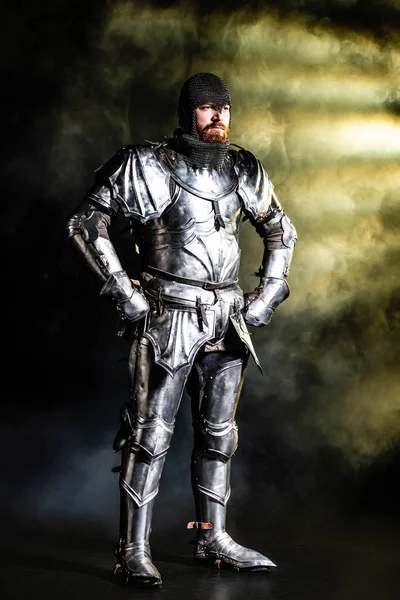 英俊的装甲骑士 双手放在黑色背景的臀上 望着远方 — 图库照片