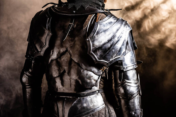 cropped view of knight in armor on black background