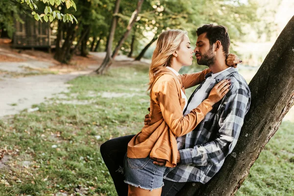 Atraente Jovem Mulher Beijando Namorado Enquanto Árvore Tronco Parque — Fotografia de Stock