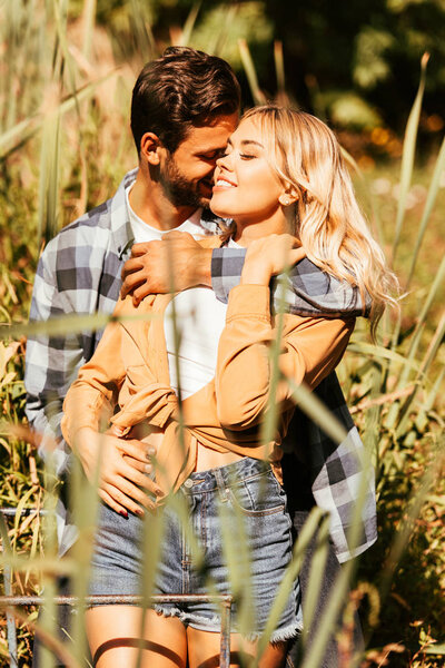 Молодой человек обнимает счастливую девушку в кустах сажи в парке
