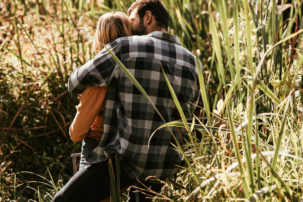 back view of man in plaid shirt embracing girlfriend in thicket of sedge 