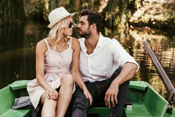 happy young couple kissing while sitting in boat on lake