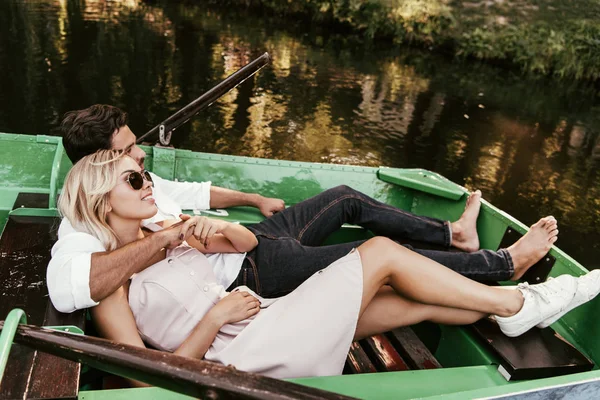happy young couple relaxing while lying in boat on lake