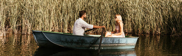 panoramic shot of young couple in boat on river near thicket of sedge