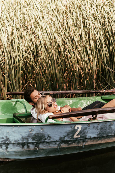 young couple relaxing in boat on river near thicket of sedge