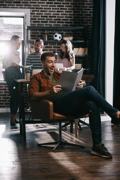 Alegre Hombre Negocios Sentado Sillón Documento Lectura Cerca Jóvenes Colegas — Foto de Stock