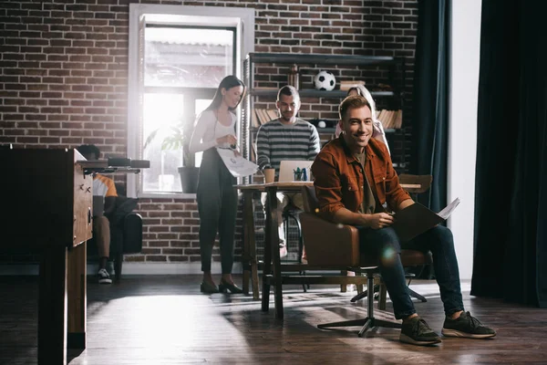 Alegre Hombre Negocios Sentado Sillón Sonriendo Cámara Cerca Jóvenes Colegas — Foto de Stock