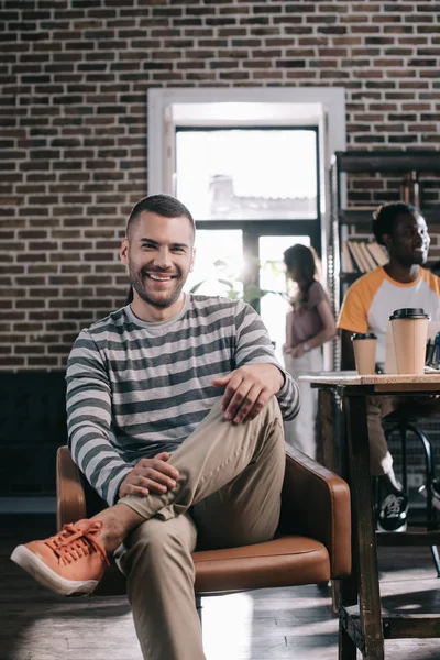 Guapo Hombre Negocios Sonriendo Cámara Mientras Está Sentado Sillón Cerca — Foto de Stock