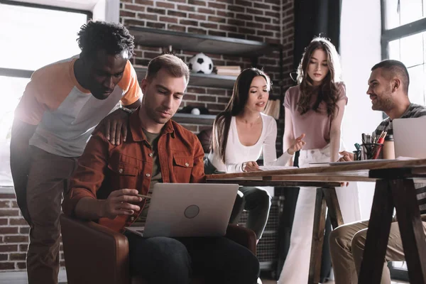 Jovem Empresário Usando Laptop Enquanto Sentado Poltrona Perto Colegas Multiculturais — Fotografia de Stock