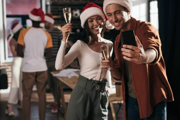 戴着桑塔帽的快乐商人和女商人拿着香槟酒酒杯在智能手机上自私自利的选择性焦点 — 图库照片
