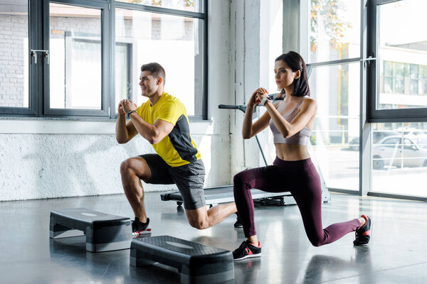 улыбающийся спортсмен и спортсменка, делающие выпады в спорткомплексе
