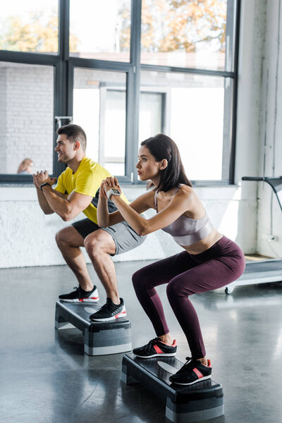 sportsman and sportswoman doing squat on step platforms in sports center