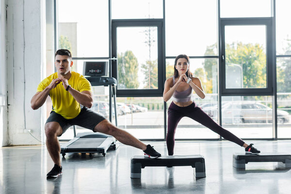 handsome sportsman and sportswoman doing lunges on step platforms in sports center