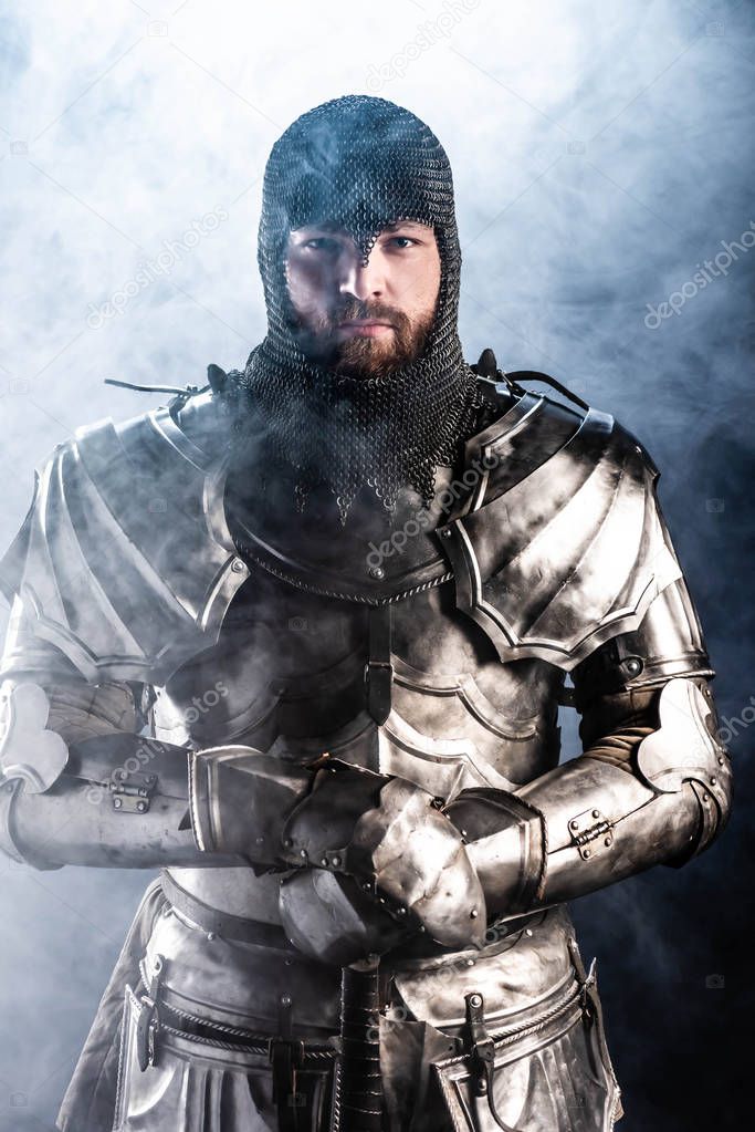 handsome knight in armor looking at camera on black background 