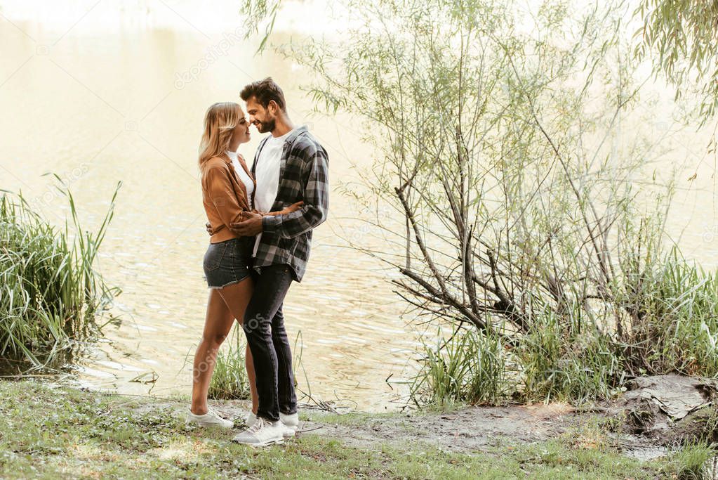 happy young couple embracing while standing near lake in park