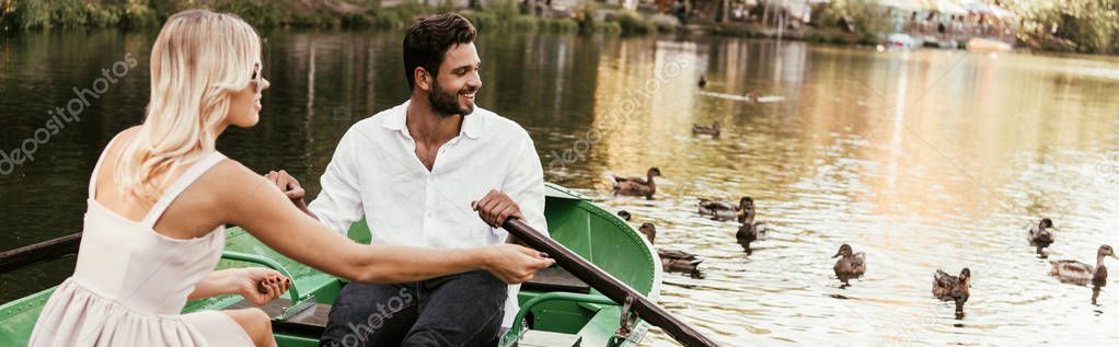 panoramic shot of young couple in boat on lake near flock of ducks