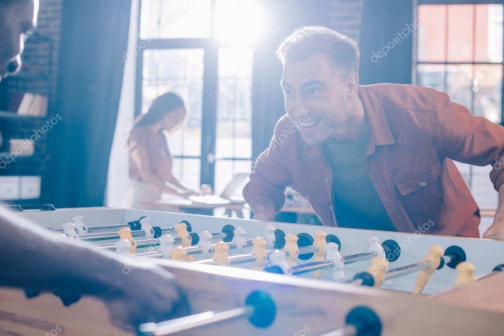 cheerful multicultural businesspeople playing table soccer in office
