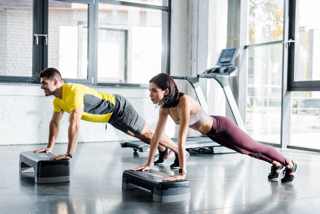 handsome sportsman and sportswoman doing plank on step platforms in sports center