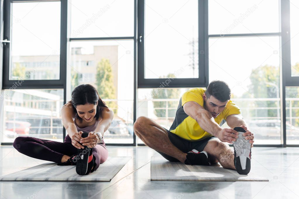 sportsman and sportswoman stretching on fitness mats in sports center