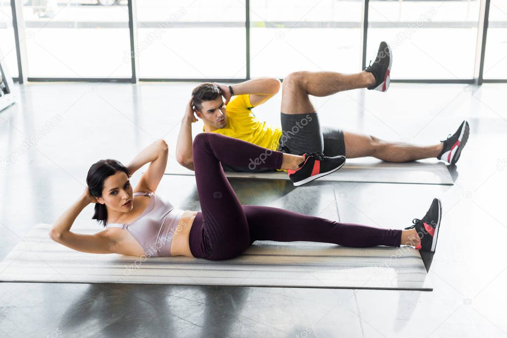 sportsman and sportswoman doing crunches on fitness mats in sports center