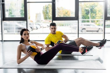 sportsman and sportswoman doing crunches with balls on fitness mats in sports center clipart