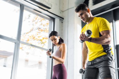 Sporcu ve sporcu kadın spor merkezinde dambıllarla çalışıyor.