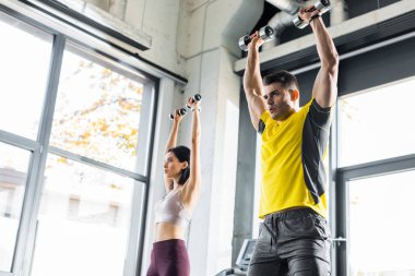 Sporcu ve sporcu kadın spor merkezinde dambıllarla çalışıyor.