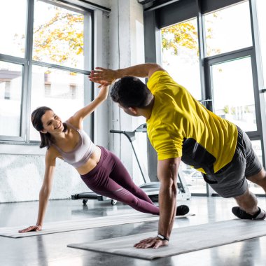 Sporcu ve gülümseyen sporcu kadın spor merkezinde kalas yapıyor ve spor minderleri üzerinde alkışlıyorlar.