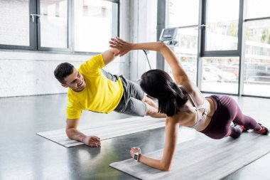 Gülümseyen sporcu ve sporcu kadın spor merkezinde kalas yapıyor ve spor minderleri üzerinde alkışlıyorlar.