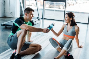 Gülümseyen sporcu spor merkezindeki kadın sporcuya bir şişe verdi.