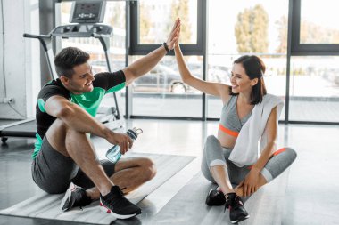 Sporcu ve sporcu kadın spor merkezinde oturup beşlik çakıyor.