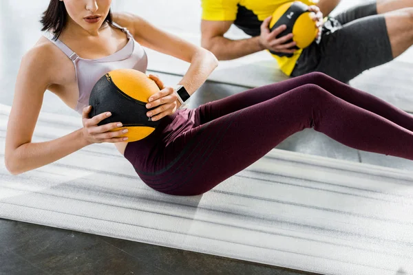 在体育中心 看到运动员和女运动员拿着健身垫上的球在做仰卧起坐 — 图库照片