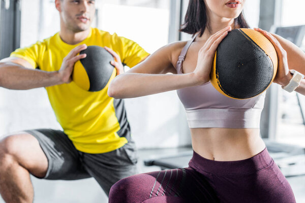 cropped view of sportsman and sportswoman doing lunges with balls in sports center