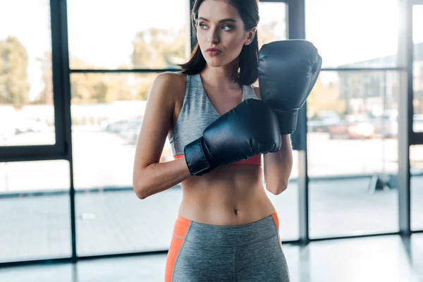 sportswoman in boxing gloves looking away in sports center