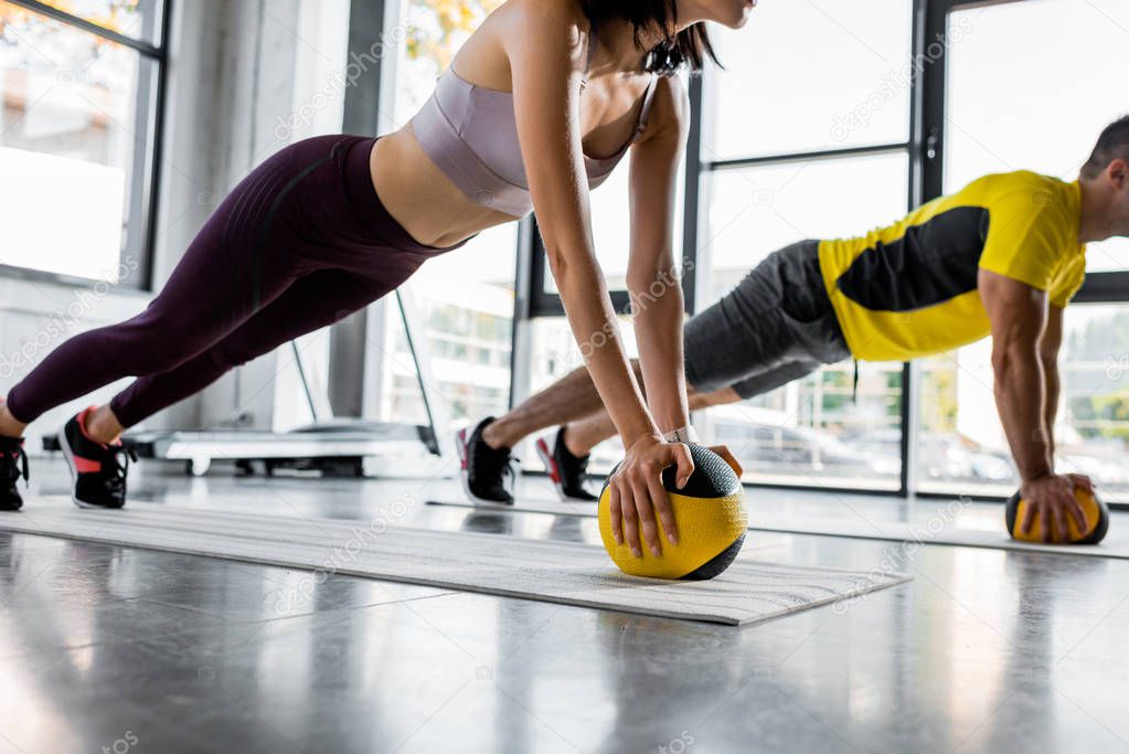 cropped view of sportsman and sportswoman doing plank with balls in sports center