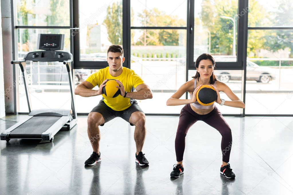 sportsman and sportswoman doing squat with balls in sports center