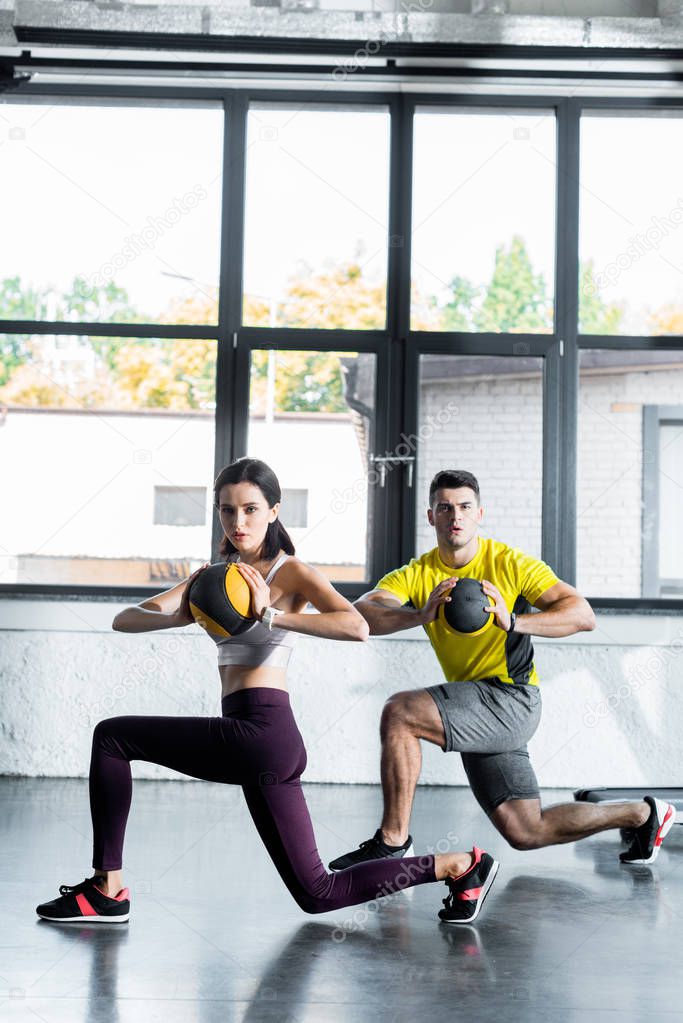 sportsman and sportswoman doing lunges with balls in sports center