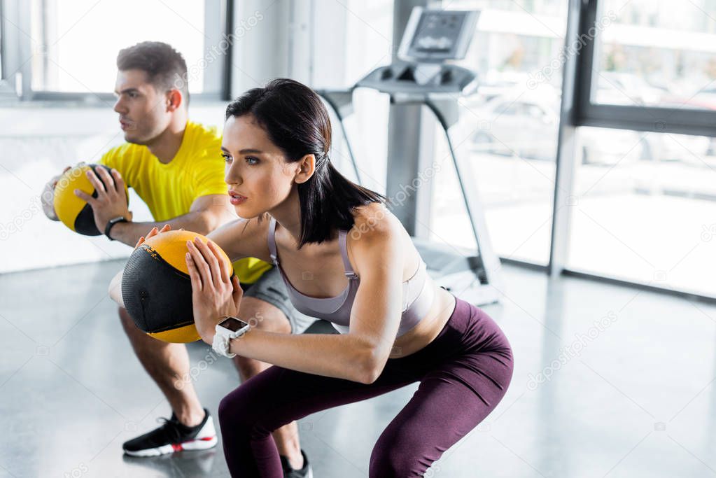 sportsman and sportswoman doing squat with balls in sports center