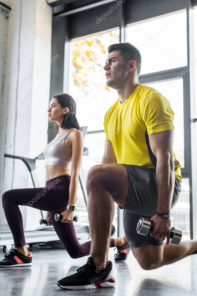 sportsman and sportswoman doing lunges with dumbbells in sports center