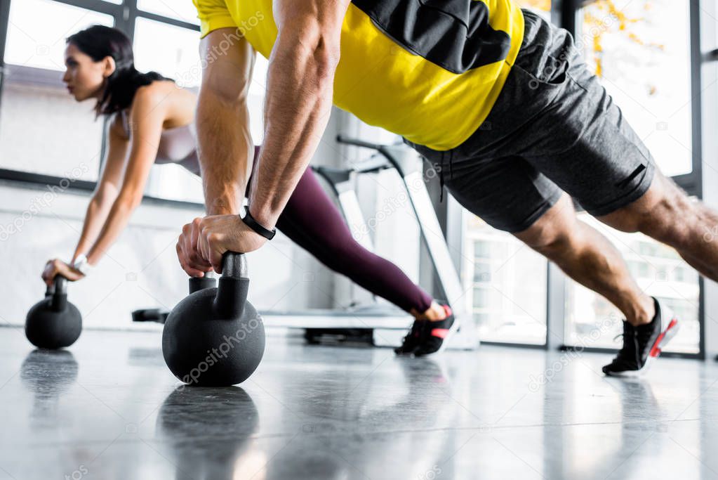 cropped view of sportsman and sportswoman doing plank on weights in sports center
