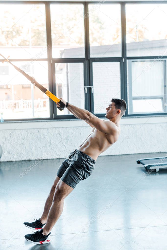 side view of handsome sportsman working out on suspension trainer in sports center 