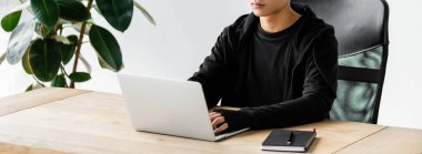 Hacker 'ın masada oturup dizüstü bilgisayar kullanmasının panoramik görüntüsü. 