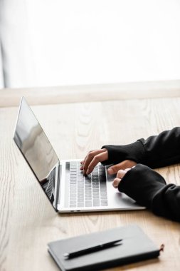 cropped view of hacker sitting at table and using laptop  clipart