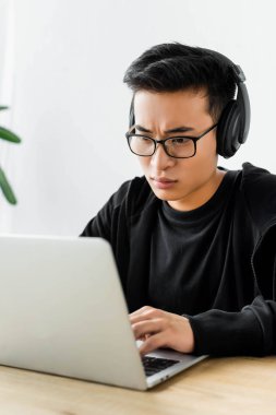 Kulaklıklı Asyalı hacker dizüstü bilgisayar kullanıyor ve masada oturuyor. 