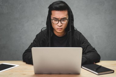 Gözlüklü Asyalı hacker dizüstü bilgisayar kullanıyor ve masada oturuyor. 
