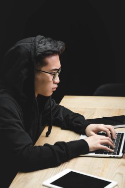 Asyalı hackerın dizüstü bilgisayarını kullanırken ve masada otururken yan görüntüsü 