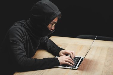 Laptop kullanan ve masada oturan Asyalı hackerın yüksek açılı görüntüsü 