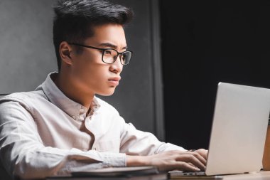 Asya seo yöneticisi masada oturuyor ve dizüstü bilgisayar kullanıyor. 